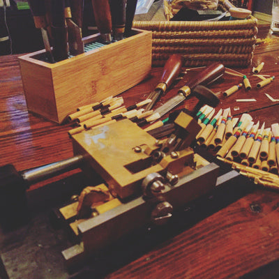 oboe reed gouging machine with oboe reeds and oboe reed knives behind.